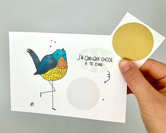 Carte postale de format A6 (classique). Un oiseau au ventre jaune, la tête bleue claire et les ailes et la queue bleus marine. Il y a le message "j'ai quelque chose à te dire" et dessous un rond gris clair sur lequel on peut écrire un mot. Ensuite un sticker qui est fourni, est à coller sur le mot et la personne qui reçoit la carte n'a plus qu'à gratter le sticker pour découvrir le message.