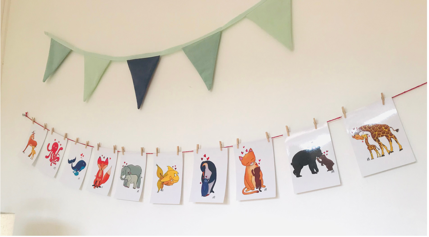guirlande à accrocher au mur avec un fil sur lequel on accroche à l'aide de petites pinces à linge dix illustrations : Dix illustrations représentant des animaux avec leurs petits. Un éléphant et son petit, un pingouin et son petit, un renard et son petit, une biche et son petit, un ours et son petit, une girafe et son petit, une pieuvre et son petit, une baleine et son petit, un poisson et son petit et enfin un chat et son petit